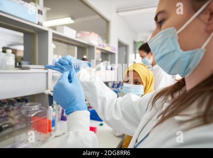 Scienziati femminili in maschere facciali e guanti di gomma che esaminano i campioni Foto Stock