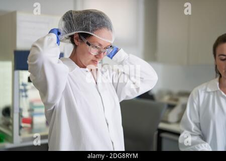 Scienziato femminile che mette su rete protettiva per capelli in laboratorio Foto Stock