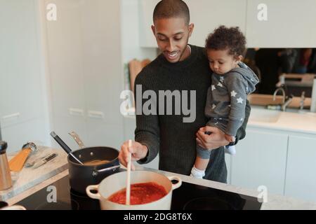 Felice padre che tiene la figlia del bambino e cucinando gli spaghetti alla stufa Foto Stock