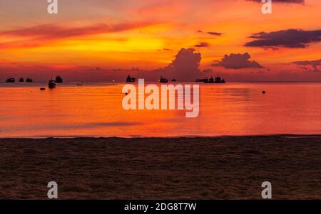 Koh Tao, Thailandia: Aprile 23 2019: isola spiaggia costa, cielo rosso e acqua dopo il tramonto del sole, colore luminoso tonalità arancio tramonto, navi e barche in t Foto Stock