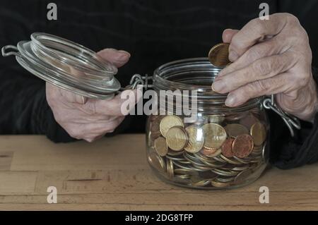 Mani di una vecchia donna che tiene un vaso di muratore con le monete. Foto Stock