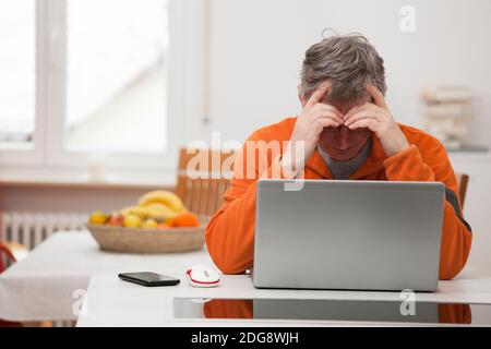 Uomo maturo stanco che lavora a casa con notebook e smart telefono - mettere a fuoco sulla testa Foto Stock