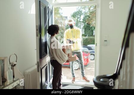 Donna che riceve il pacchetto dall'uomo di consegna in maschera di faccia a. sportello anteriore Foto Stock