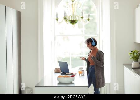 Donna con cuffie per videoconferenze al computer portatile in cucina Foto Stock