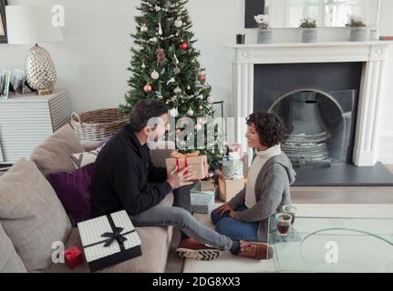 Marito che dà il regalo di Natale a moglie da albero in vita camera Foto Stock