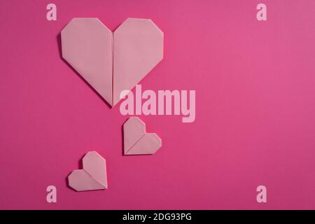 Origami cuori realizzati con carta colorata per congratulazioni per San Valentino per coppie innamorate, su sfondo rosa. Concetto di amore Foto Stock