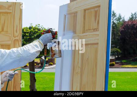 Primo piano della pistola a spruzzo con verniciatura Master verniciatura porte in legno. Foto Stock