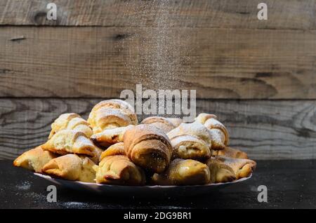 Biscotti fatti in casa sotto forma di bagel con marmellata di ripieno cosparso di zucchero in polvere su uno sfondo di legno. Messa a fuoco selettiva. Foto Stock