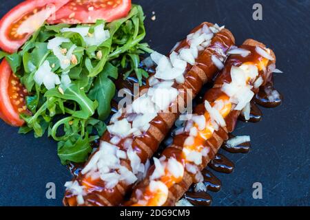 Cibo a base di spazzatura americana in una composizione semplice. Salsicce fritte croccanti o hot dog con salsa mayo e ketchup e cipolla tritata. Alcune verdure intorno lik Foto Stock