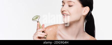 sorridente giovane bella donna con vitiligo che tiene rullo di giada sopra faccia isolata Foto Stock