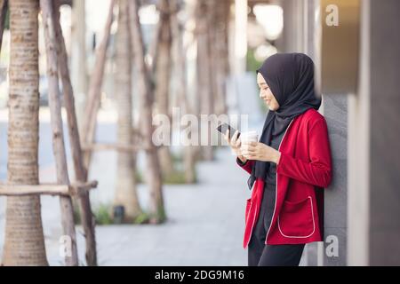 Operazione riuscita. Donne arabe d'affari in hijab tenere un caffè per strada e tenere un telefono cellulare Foto Stock