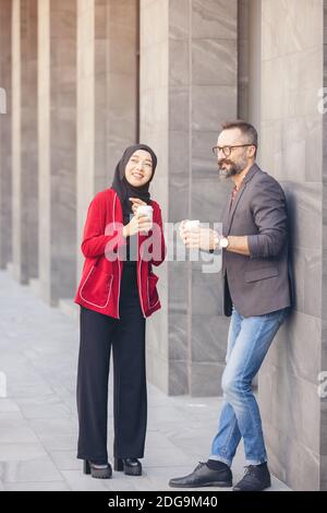 Bella barba di mezza età uomo d'affari caucasico bere caffè all'aperto caffè con giovani belle donne musulmane hijab Foto Stock