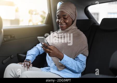 Donna d'affari musulmana nera in hijab che usa lo smartphone durante i viaggi in auto Foto Stock