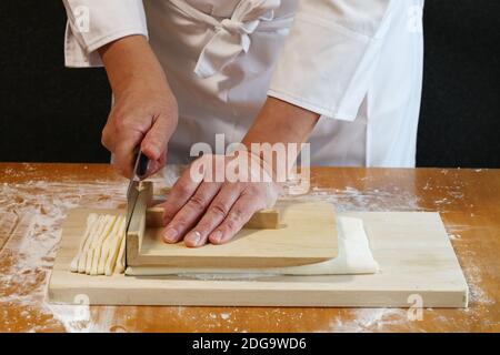 come fare gli udon giapponesi; tagliare la pasta arrotolata con un coltello. Foto Stock