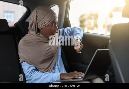 Essere in ritardo. Stressed Businesswoman musulmano nero seduta in taxi e tempo di controllo Foto Stock