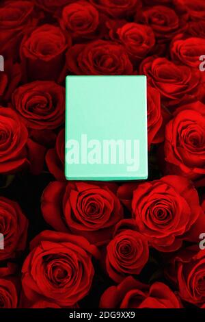 scatola regalo turchese per gioielli su un bouquet di rose rosse flatlay. Foto Stock