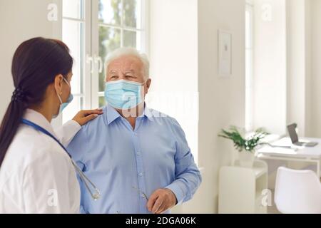 Donna medico che tocca la spalla del paziente anziano maturo dell'uomo dentro maschera dopo visita in clinica Foto Stock