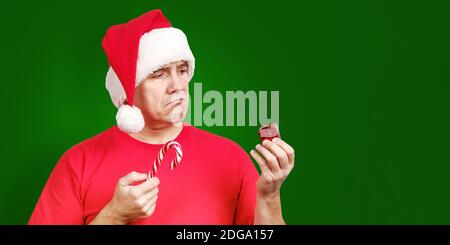 Uomo in cappello di Santa con canna caramella in mano Contiene il piccolo regalo di Natale difettoso Foto Stock