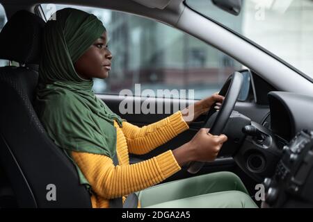 Giovane conducente. Grave donna musulmana nero guida auto focalizzata sulla strada Foto Stock
