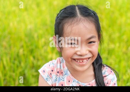 Bel ritratto di bambina asiatica in vacanza, viso carino con grande sorriso, capelli neri lunghi, primo piano taglio faccia, sfondo sfocato campo di riso. Spazio Foto Stock