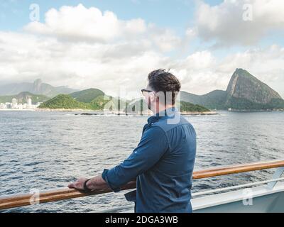 Uomo alla moda sul ponte vuoto di una nave da crociera sullo sfondo di onde marine. Vista laterale, primo piano. Concetto di svago e di viaggio Foto Stock