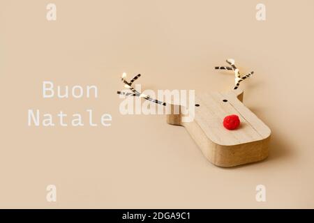 una divertente testa di renna in legno, con un naso rosso, e il testo buon natale in italiano su uno sfondo marrone chiaro Foto Stock