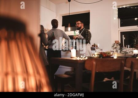 Gruppo sorridente di amici diversi che parlano insieme in cucina oltre le bevande prima di una cena di festa Foto Stock