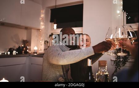 Una coppia sorridente che brinda gli amici con il vino mentre si siede insieme a. a tavola durante una cena a lume di candela Foto Stock