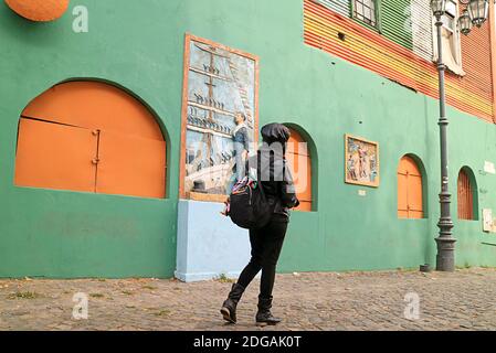 Donna camminando lungo il colore vivace dipinti vecchi edifici nel quartiere la Boca, Buenos Aires, Argentina, Sud America Foto Stock