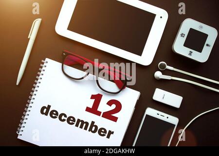 12 dicembre. Giorno 12 del mese, data del calendario. Ambiente di lavoro in ufficio con notebook, notebook, forniture per ufficio e cancelleria sul retro marrone. Mese invernale, giorno Foto Stock