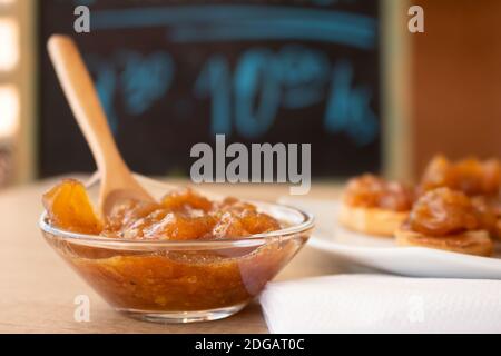 Pentola di vetro con un delizioso chutney fatto in casa di mele e cipolle, con cannella su un pannello di legno chiaro. Marmellata perfetta per la colazione. Colazione, cucina Foto Stock