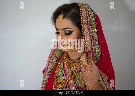 Una bella ragazza indiana in abito da sposa con saree rosse e ornamenti d'oro Foto Stock