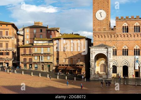 Vista ravvicinata della base della Torre del Mangia e degli edifici circostanti immersi nella luce dorata, Siena, Toscana, Italia Foto Stock