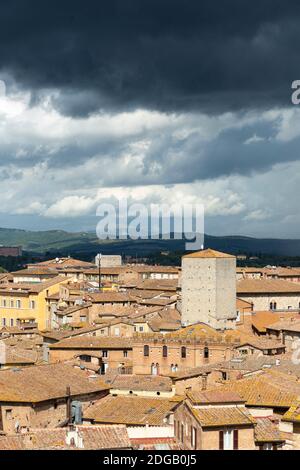 Vista dal paesaggio urbano che mostra la torre medievale sotto le nuvole buie della tempesta, come si vede da Facciatone, Siena, Toscana, Italia Foto Stock