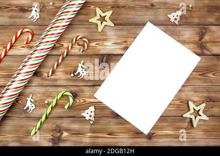Decorazioni natalizie, carta da imballaggio, canne caramelle, un foglio bianco di carta su sfondo di legno. Disposizione piatta. Foto Stock