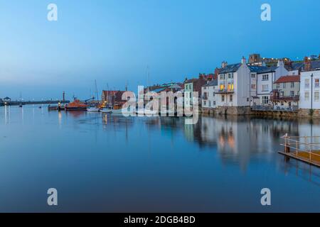 Vista delle barche e delle case che si riflettono nel fiume Esk al tramonto, Whitby, Yorkshire, Inghilterra, Regno Unito, Europa Foto Stock