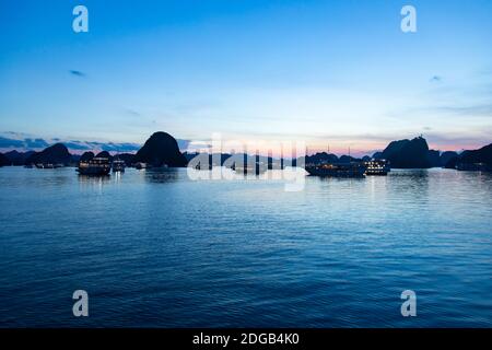 Dopo il tramonto, ammira la baia di ha Long, un sito patrimonio dell'umanità dell'UNESCO. Ogni giorno le navi da crociera navigano nel complesso roccioso pieno di turisti Foto Stock