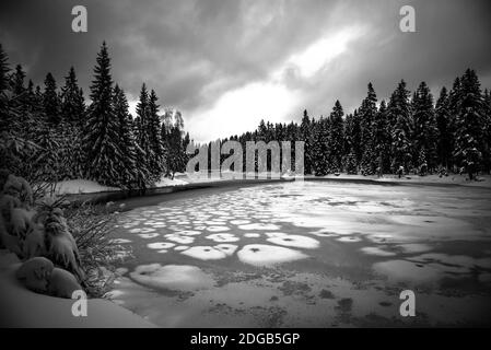 Inverno ghiacciato a stagno congelato. Paesaggio innevato. Blatny Water Reservoir in Jizera Mountains, Repubblica Ceca immagine in bianco e nero. Foto Stock