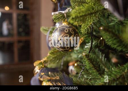 Messa a fuoco selettiva. Palla nera di Natale su un albero di Natale dorato. Giocattoli di Natale, regali in una scatola nera e d'oro e ghirlande di luci. Foto Stock