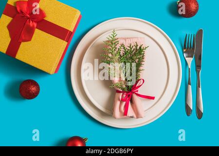 Tavolo servito con piatto e posate per la celebrazione di Natale e Capodanno. Sul piatto è tovagliolo con un ramo dell'albero di Natale, palline rosse. Flatlay ON Foto Stock