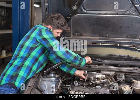 Bel meccanico che parla al telefono mentre ripara un'auto . Foto Stock