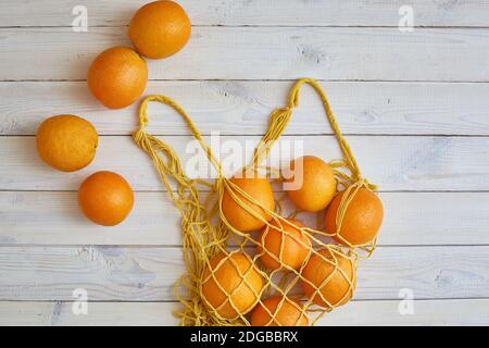 Vista dall'alto di arance fresche nella stringa borsa in bianco sullo sfondo rustico Foto Stock