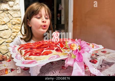 Giovane ragazza che soffia le candele su torta di fragole di ottavo compleanno Foto Stock