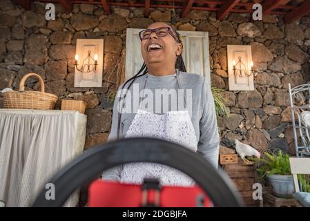 donna nera con gli occhiali insegna online con il suo telefono cellulare lezioni di cucina da casa Foto Stock