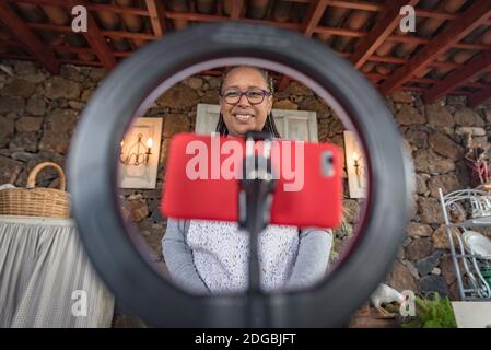 donna nera con gli occhiali insegna online con il suo telefono cellulare lezioni di cucina da casa Foto Stock