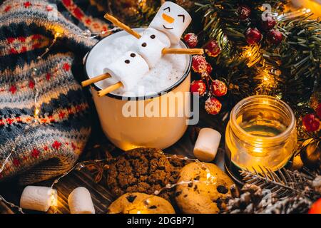 Tazza bianca di cibo di Natale con marshmallows di pupazzo di neve al cioccolato caldo. Biscotti fatti in casa, bastoni di cannella rami di abete xmas con luci calde di ghirlanda. Est Foto Stock