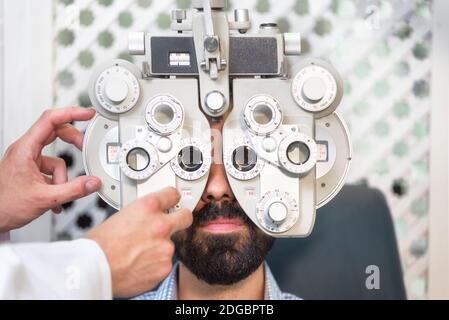 L'optometrico che fa il controllo della vista per il paziente maschio in clinica. Oftalmologo maschile che esamina l'uomo del paziente con uno studio di optometristo fr Foto Stock