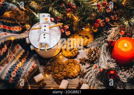 Tazza bianca di cibo di festa con marshmallows caldi del pupazzo di neve del cacao del cioccolato. Biscotti dolci fatti in casa, bastoni della cannella rami dell'albero di abete xmas con garland caldo Foto Stock