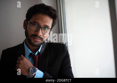 Ritratto di un giovane bruna indiano alto, scuro e bello in abbigliamento da ufficio è in piedi davanti a una finestra di vetro in un ufficio aziendale/bpo Foto Stock