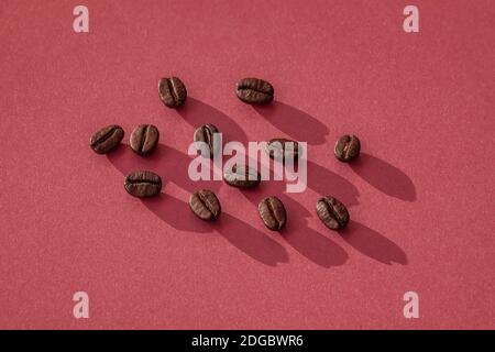 Sfondo di colore borgogna con grani tostati di caffè scuro, vista dall'alto. Concetto di colazione e pausa caffè. Foto Stock